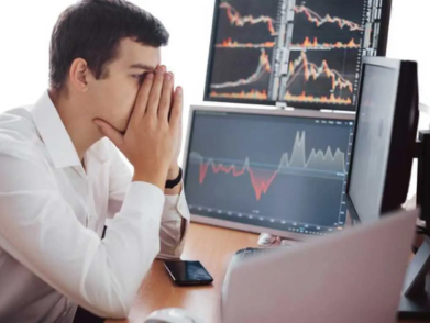 A frustrated man sits at a desk in front of multiple computer screens, appearing stressed and in need of IT support.